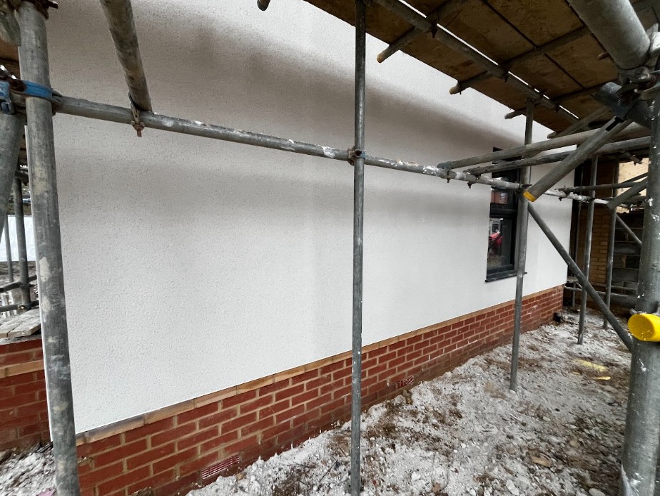 A heavy monocouche scraping tool being passed over cured single-coat render to expose its light reflective lime-like texture