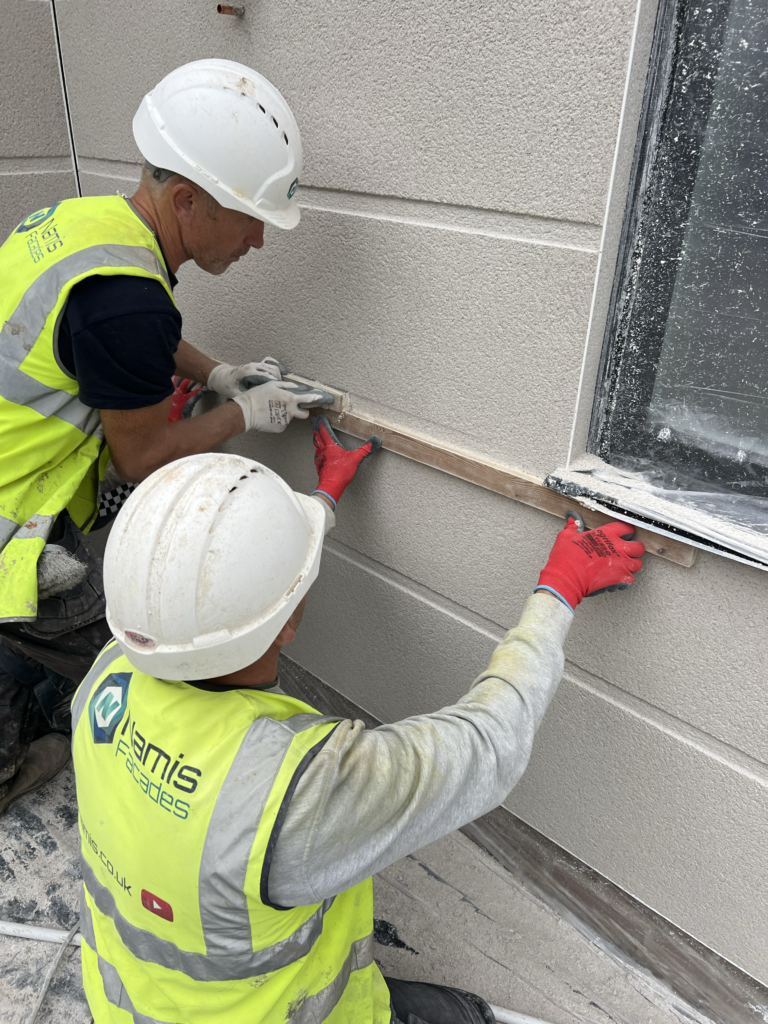 A professional UK plasterer trowelling a base coat of traditional sand and cement mix directly to a brick masonry house extension wall
